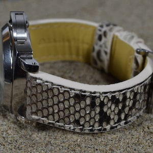 Peut inclure: Une montre argentée avec un bracelet en cuir de serpent blanc et brun.