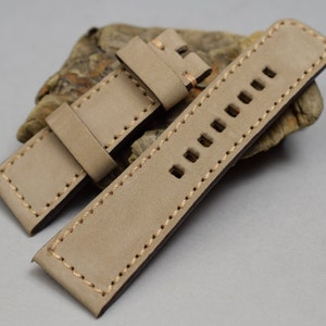 Puede incluir: Una correa de reloj de cuero marrón claro con costuras blancas y múltiples agujeros para ajustar el tamaño.