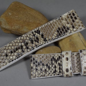 Può includere: Un cinturino da orologio bianco con un motivo a pelle di serpente marrone e nero. Il cinturino ha una fibbia ed è in pelle.