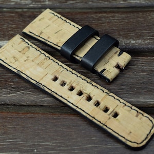 May include: A watch strap made of cork with black leather accents. The strap has a stitched edge and is designed for a watch with spring bars.
