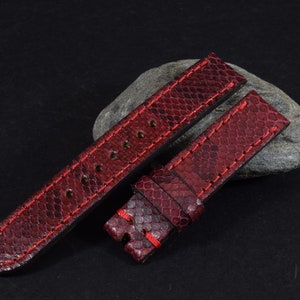 Op de afbeelding: Bordeaux horlogebandjes met een slangenleertextuur en rode stiksels. De bandjes zijn gemaakt van een textuurrijk materiaal en worden op een donkere achtergrond gepresenteerd.