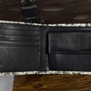 May include: A black leather wallet with multiple card slots and a billfold. The wallet is made of genuine snakeskin and has a subtle pattern.