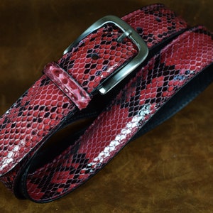 May include: A red snakeskin belt with a silver buckle. The belt is made of genuine leather and has a classic design.