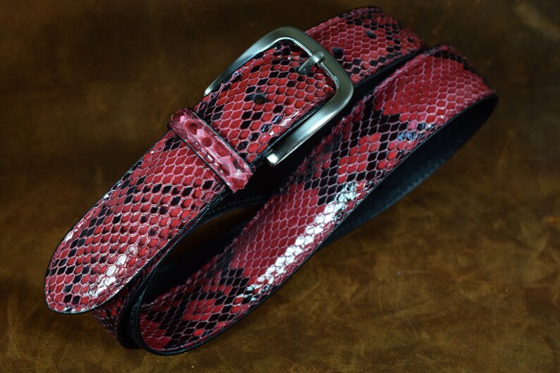 May include: A red snakeskin belt with a silver buckle. The belt is made of genuine leather and has a classic design.