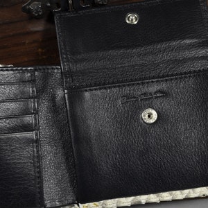 Pode incluir: Uma carteira de couro preta com v&aacute;rios slots para cart&otilde;es e um porta-notas. A carteira est&aacute; aberta para revelar um interior de couro preto com um fecho de press&atilde;o. A carteira &eacute; feita de couro genu&iacute;no e tem um padr&atilde;o de pele de cobra.