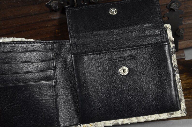 Pode incluir: Uma carteira de couro preta com v&aacute;rios slots para cart&otilde;es e um porta-notas. A carteira est&aacute; aberta para revelar um interior de couro preto com um fecho de press&atilde;o. A carteira &eacute; feita de couro genu&iacute;no e tem um padr&atilde;o de pele de cobra.