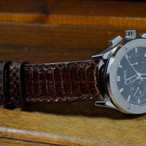 Może przedstawiać: Srebrny zegarek naręczny z chronografem, z czarną tarczą i brązowym skórzanym paskiem. Zegarek posiada datownik i skalę tachymetru.