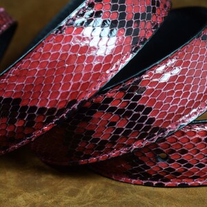 May include: A close-up of a red and black snakeskin belt. The belt is made of genuine leather and has a unique, textured pattern.
