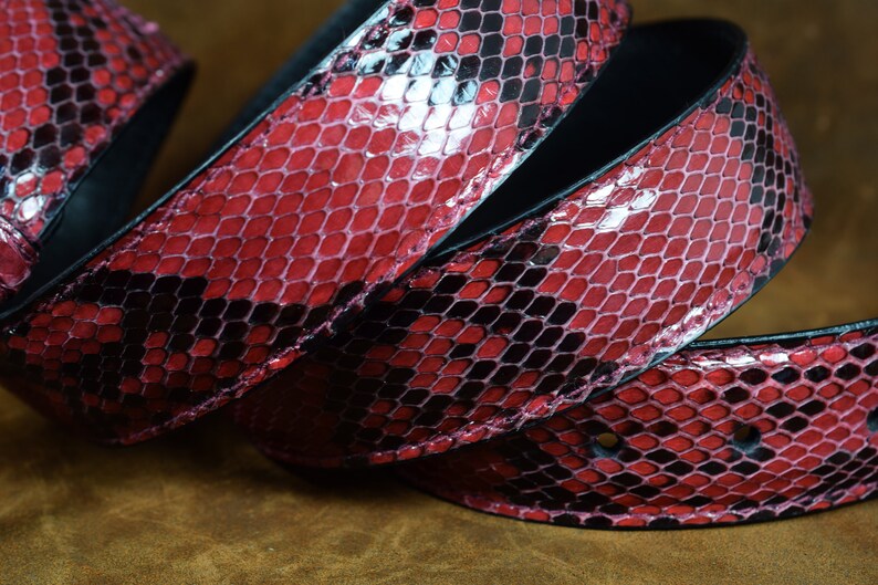 May include: A close-up of a red and black snakeskin belt. The belt is made of genuine leather and has a unique, textured pattern.