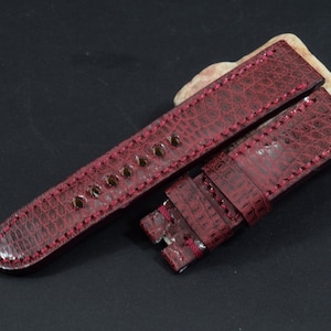 May include: A red leather watch strap with a textured pattern. The strap is stitched with red thread and has a buckle.