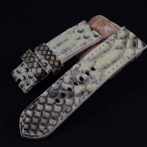 Op de afbeelding: Twee horlogebandjes gemaakt van wit en grijs slangenleer. De bandjes zijn met wit garen aan elkaar gestikt en hebben een textuur.