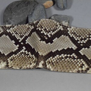 K&ouml;nnte beinhalten: Eine braune und beige Schlangenleder-Geldb&ouml;rse mit einer Klappverschluss.