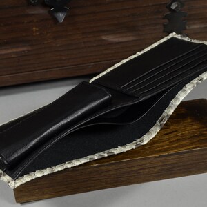 Pode incluir: Uma carteira de couro preta com v&aacute;rios slots para cart&otilde;es e um porta-notas. A carteira &eacute; forrada com um material de pele de cobra cinza claro.