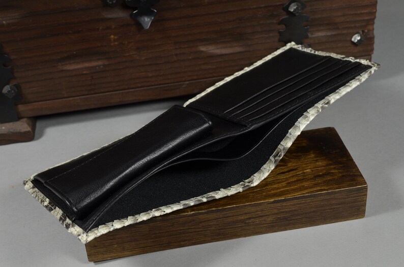 Pode incluir: Uma carteira de couro preta com v&aacute;rios slots para cart&otilde;es e um porta-notas. A carteira &eacute; forrada com um material de pele de cobra cinza claro.