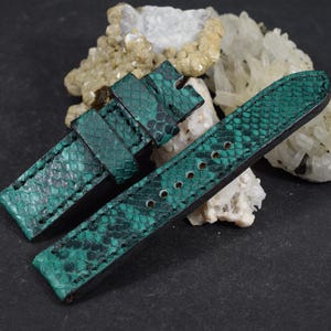 May include: A two-piece watch strap featuring a textured, emerald green snakeskin pattern with black stitching. The strap includes a buckle end with a fixed loop and a long end with multiple circular adjustment holes for a secure fit.