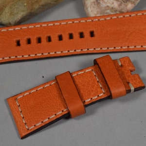 Könnte beinhalten: Orangefarbenes Lederarmband mit weißen Nähten. Das Armband hat eine Schließe und ist für eine Uhr mit einem Schnellverschluss-Federsteg konzipiert.