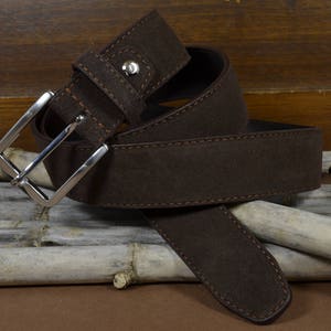 May include: A brown leather belt with a silver buckle. The belt is folded and lying on a wooden surface.