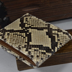 May include: A brown leather wallet with a snakeskin pattern. The wallet is folded in half and has a brown leather flap.