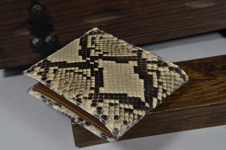 May include: A brown leather wallet with a snakeskin pattern. The wallet is folded in half and has a brown leather flap.
