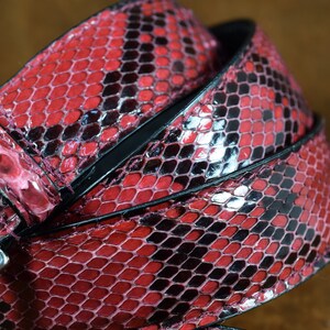 May include: A red and black snakeskin belt with a silver buckle.