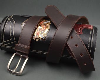 May include: A dark brown leather belt with a silver buckle is wrapped around a black leather cylindrical case. The case has white stitching and a gold emblem. The belt has several holes for adjustment.