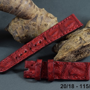 May include: Red watch straps made of textured leather. The straps are in two pieces, with a buckle and several holes for adjustment. The text "20/18 - 115/75 mm" is visible. The straps are displayed against a neutral background.