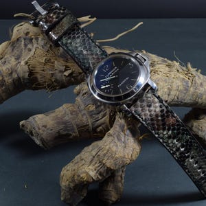 Può includere: Un orologio in acciaio inossidabile con quadrante nero e cinturino con motivo a pelle di serpente. Il quadrante mostra le parole "Luminor Marina" e "Panerai". Il cinturino è un mix di verde, marrone e nero.