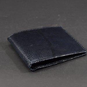 Puede incluir: Una cartera de cuero negra con un patrón texturizado que parece piel de serpiente.