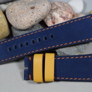 Op de afbeelding: Een donkerblauwe leren horlogeband met oranje stiksels en een gele leren keeper. De band heeft zeven gaten om de maat aan te passen.