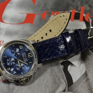 May include: A blue chronograph watch with a stainless steel case and a navy blue leather strap. The watch face features white markings and the text "MAFINA MILITARE CHRONOGRAPH".