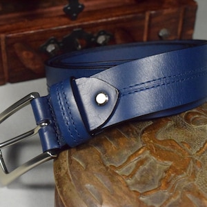 May include: A blue leather belt with a silver buckle. The belt has a single stitch down the center and is folded over on itself.