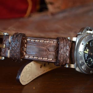 May include: A brown leather watch strap with a stitched edge and a silver watch attached.
