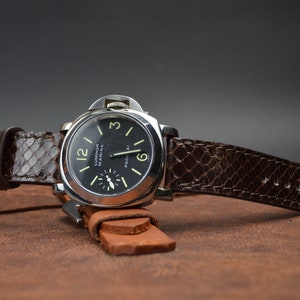 May include: A brown leather watch strap with a black watch face that reads "Luminor Marina Panerai".