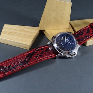 Peut inclure: Un bracelet de montre en peau de serpent rouge et noir avec un cadran de montre argenté qui indique "Luminor Marina Panerai".