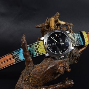 Op de afbeelding: Een zwart horloge met een zilveren band en een multi-kleurige slangenleren band. De wijzerplaat van het horloge heeft witte cijfers en wijzers, en de woorden "Luminor Marina" en "Panerai" zijn op de wijzerplaat gedrukt.