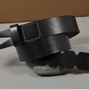 May include: A black leather belt with a triangular buckle and a stitched square on the strap. The belt is folded and the buckle is on the right side of the image.