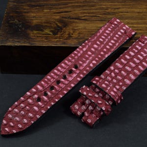 Op de afbeelding: Een rood leren horlogebandje met een textuurpatroon. Het bandje is gemaakt van echt leer en heeft een klassiek ontwerp.