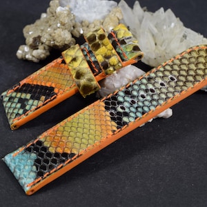 May include: A watch strap featuring a textured snakeskin pattern in vibrant shades of yellow, orange, black, and turquoise. The strap is finished with bright orange leather edges and includes a matching sliding keeper loop.