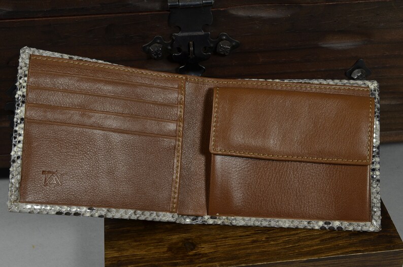 May include: Open brown leather wallet with a snakeskin trim. The wallet has multiple card slots and a coin pocket. The interior is brown leather, and the exterior trim is black, white, and grey.