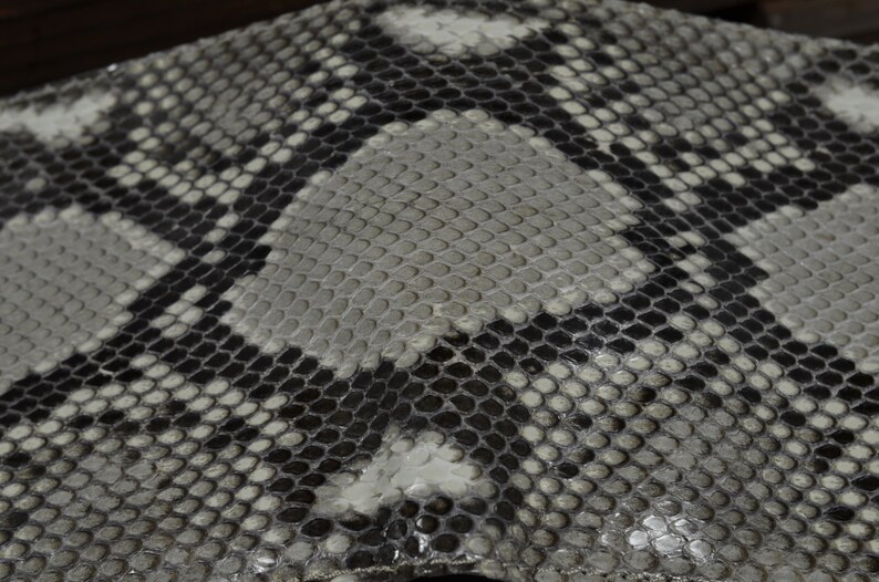 May include: Close-up of a textured surface with a snakeskin pattern. The design features a repeating pattern of scales in shades of grey, black, and white. The scales are small and tightly packed, creating a detailed and visually interesting texture.