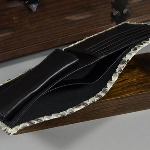 May include: A black leather wallet with multiple card slots and a billfold. The wallet is made of genuine snakeskin and has a light brown colour.