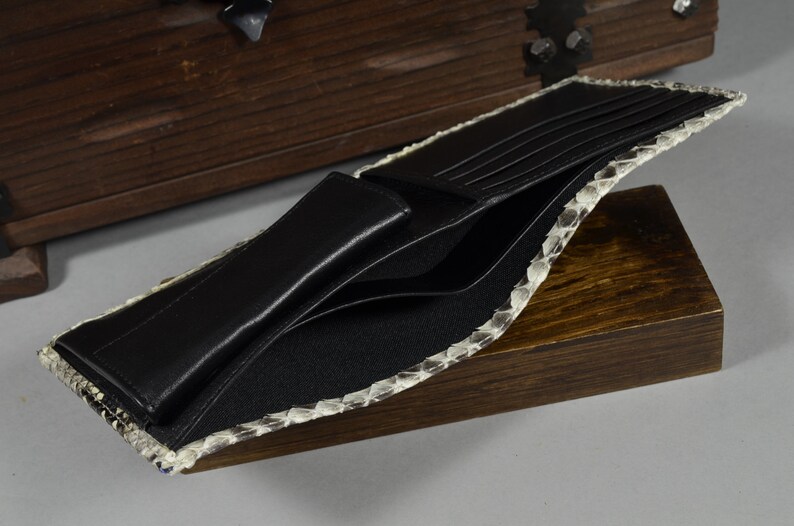 May include: A black leather wallet with multiple card slots and a billfold. The wallet is made of genuine snakeskin and has a light brown colour.