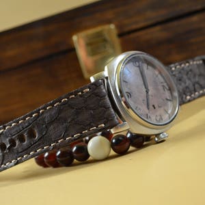 May include: A silver wristwatch with a brown leather strap featuring a textured pattern. The watch has a white face with black Roman numeral markings and a silver second hand.