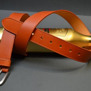 Peut inclure: Une ceinture en cuir marron enroulée autour d'une bouteille dorée avec le mot "Martini" imprimé dessus.