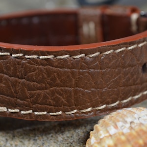 May include: A brown leather watch strap with white stitching. The strap has a textured surface that resembles elephant skin.