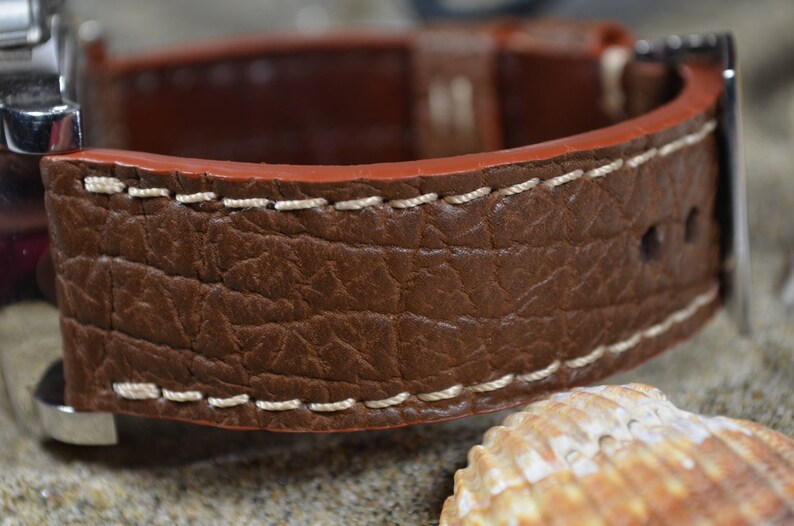 May include: A brown leather watch strap with white stitching. The strap has a textured surface that resembles elephant skin.