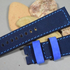 Op de afbeelding: Een donkerblauwe leren horlogeband met blauwe stiksels en een blauwe suède voering. De band heeft meerdere gaten om de maat aan te passen.