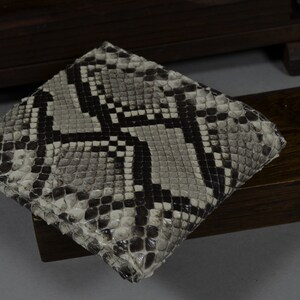 Pode incluir: Uma carteira de pele de cobra preta e branca com um padr&atilde;o texturizado.