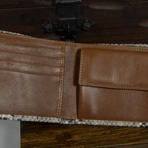 May include: Open brown leather wallet with a snakeskin trim. The wallet has multiple card slots and a coin pocket. The interior is brown leather, and the exterior trim is black, white, and grey.