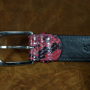 May include: A black leather belt with a silver buckle and a pink snakeskin pattern on the end.